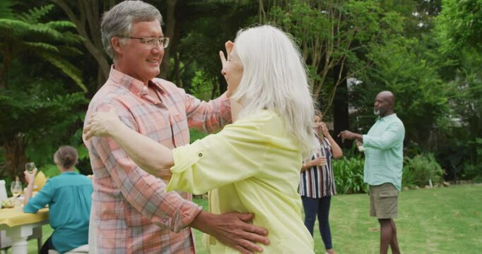 Animation of happy caucasian senior couple danging in garden while having lunch with friends