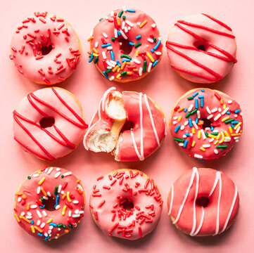 Top view of donuts with pink glaze and sprinkles on pink backdrop.