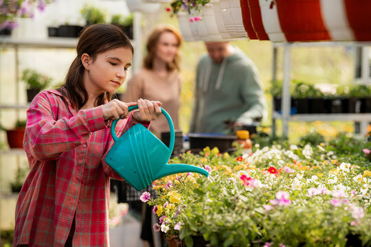 Girl Watering Plants in a Greenhouse with Family