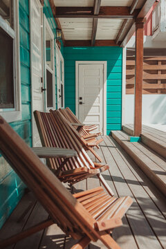 Wooden chairs lined up on a sunny porch of a teal Belize cabin