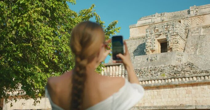 Woman photographing Mayan ruins historical stone structure during cultural travel visit