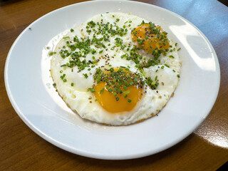 Sunny side up eggs with chives and pepper on white plate