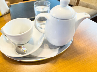 White teapot and cup on a wooden table with a glass of water