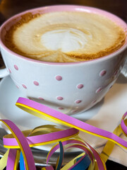 Polka dot mug with cappuccino and colorful streamers on white saucer
