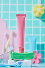 Vibrant pink and yellow toothpaste tubes next to a toothbrush and water glass with a green mosaic...