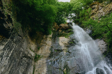 Waterfall cascading down rocky cliff surrounded by lush green forest and vibrant foliage in a...