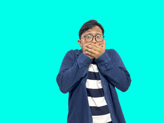 A shocked Asian man covers his mouth, eyes wide open, expressing surprise on an aqua background. Perfect for reaction, emotion, and unexpected news visuals