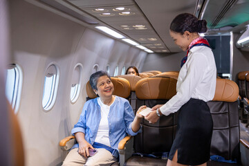 Flight attendant is welcoming and checking senior woman passenger boarding pass and show her seat for airplane flight and airline transportation