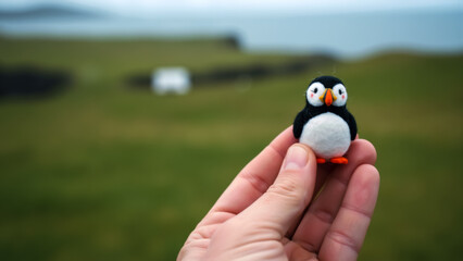 Hand holding cute felt puffin figurine souvenir in Icelandic landscape. Traditional craft and travel memory from Iceland. Icelandic wildlife symbol toy.