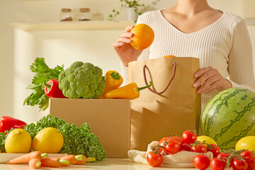 A woman picks up an orange from a paper grocery bag, surrounded by colorful and fresh produce....