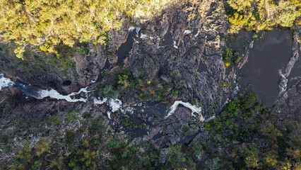 Aerial view of cascading waterfalls flowing through dense forest and rocky terrain
