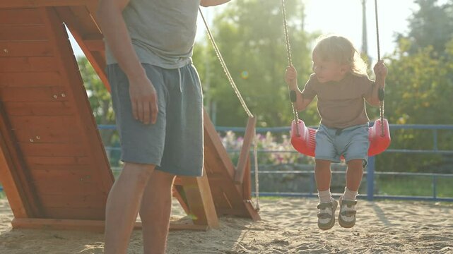 Parent pushes child on swing at playground. child enjoying swing ride outdoors. Happy bonding moment between parent and child. Family fun swing at sunny playground. Child playing with parent on swing.