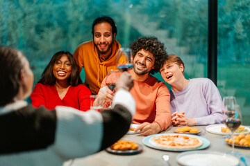 Friends toasting red wine at dinner table celebrating with pizza