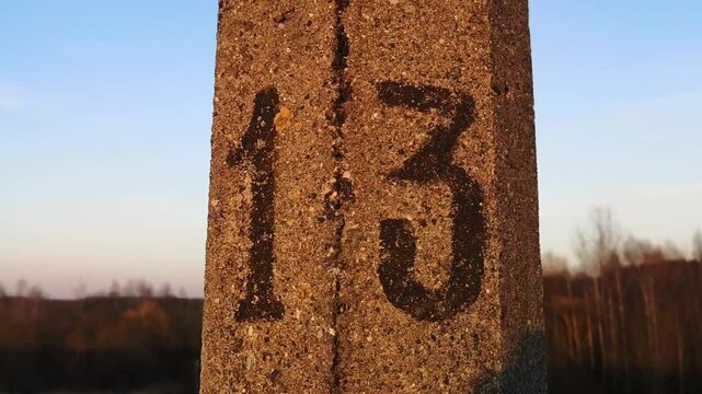 The number 13 is drawn in black paint on a pole close-up against the blue sky. Symbol of Friday the 13th. Sign. Distance marker. House number. Baker's dozen. Folk omen. Nobody. Fatalism. Numerology.