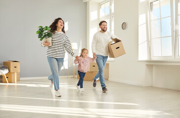Happy excited young family with child girl standing in living room at home with unpacked boxes in...