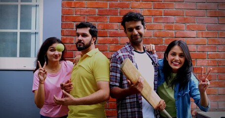 College team with bat ball posing together, Indian Asian university students smiling confidently as male and female cricket players hold bat and ball while standing against red brick campus wall - Powered by Adobe