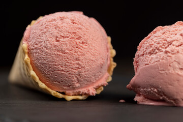 melting pink ice cream on a black slate board, sweet cold pink ice cream with strawberry flavor, ice cream in a waffle cone, close up