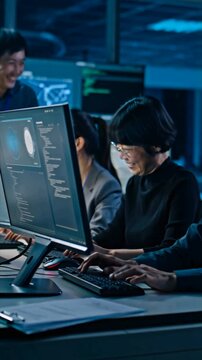 A group of Asian software developers focus on programming tasks in a contemporary office setting. They engage in teamwork, utilizing advanced technology late at night for efficient coding