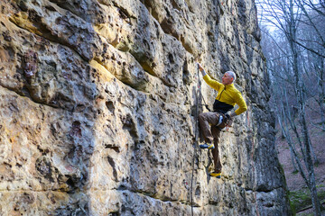 Young man climbing steep rock in nature with bottom rope