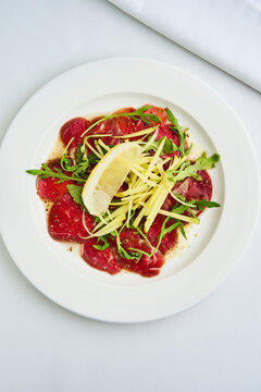 Delicious Beef Carpaccio Topped With Fresh Herbs and Citrus Served on a White Plate at a Cozy Restaurant
