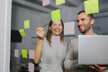 Two people collaborating in an office with sticky notes and a laptop during a brainstorming session