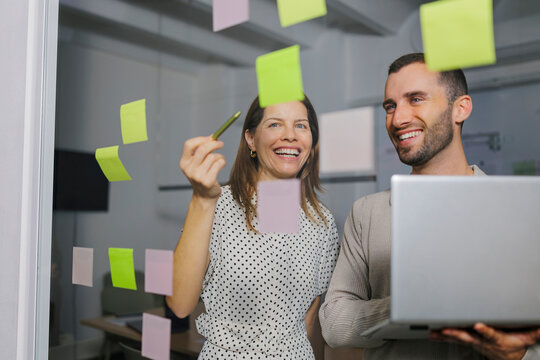 Two people collaborating in an office with sticky notes and a laptop during a brainstorming session
