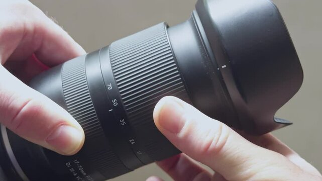 Hands hold a 17-70 mm lens with adjustable focal length, showing the scale from 17 to 70