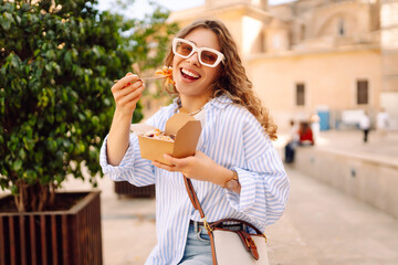 Portrait of beautiful woman eating pasta from takeaway box on the street outdoors. Young woman...