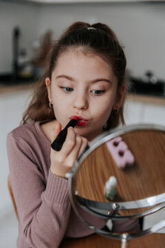 Girl applying lipstick while looking in a mirror indoors