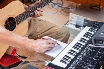 male composer writing a song on paper while playing acoustic guitar in home studio. songwriting or music education concept