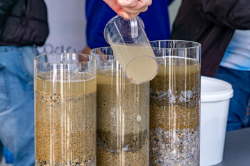 Water filtration demonstration using transparent columns filled with sand, gravel, and sediment. A...