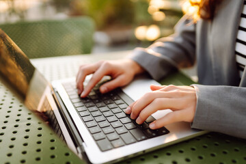 Hands of young woman typing on laptop keyboard in sunset rays. Close-up of hands of female...