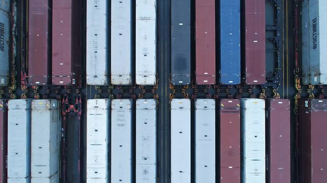 Containers of various colors are organized in rows at a busy shipping terminal. Cranes and trucks move around, highlighting the logistics operations during the day.
