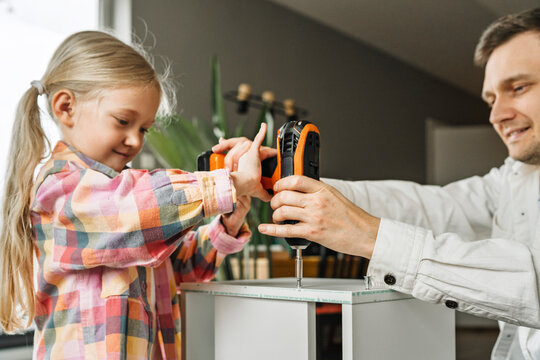 Father and daughter drilling furniture together at home, enjoying quality time and teamwork