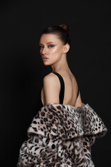 model poses confidently, emphasizing her modern fashion sense with a stylish animal print coat. dark background highlights her elegant attire and striking makeup