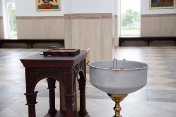The image shows a baptismal font next to a carved wooden table in the bright interior of a church....