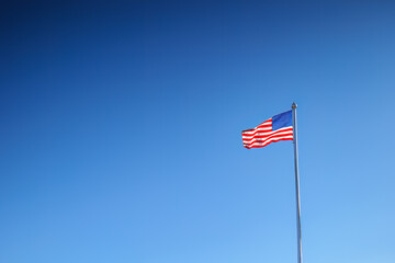 American flag waving on a flagpole against a clear blue sky