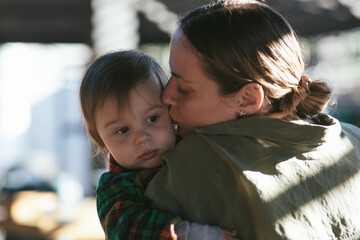 Mom and her son toddler walking in the park. Mom is kissing kid cheek, lifestyle photo. 