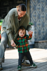 Mom and her son toddler in the park. Mom is holding kid hand, they are walking outdoor. Happy family dream concept. Mother and child together, lifestyle photo.