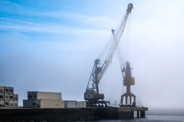 Industrial port crane and shipping containers in morning fog by