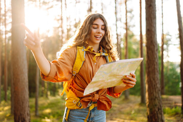 Young female hiker with bright backpack and map in hands looking for direction on hiking trail....