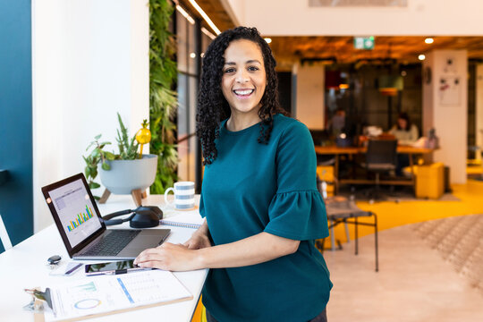 Smiling businesswoman with laptop on desk at office