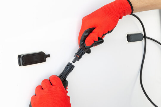 Cropped view of technician in gloves installing solar panel system. Close up of hands connecting mc4 connectors over solar panel. Renewable energy concept.