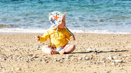 Happy baby with sun hat and UV protection enjoying at the beach
