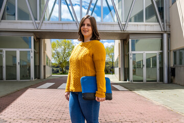 University student smiling and holding laptop case outside campus building