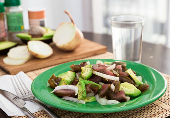 Salad of black tomatoes, avocado and onions on green plate