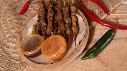 some skewers of satay and chili sauce on a wooden plate