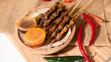 some skewers of satay and chili sauce on a wooden plate