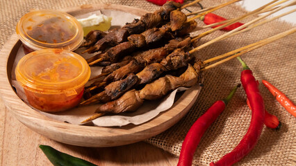 some skewers of satay and chili sauce on a wooden plate