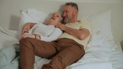 A man lies on a bed and hugs a woman who lies next to him, they laugh and talk - Powered by Adobe